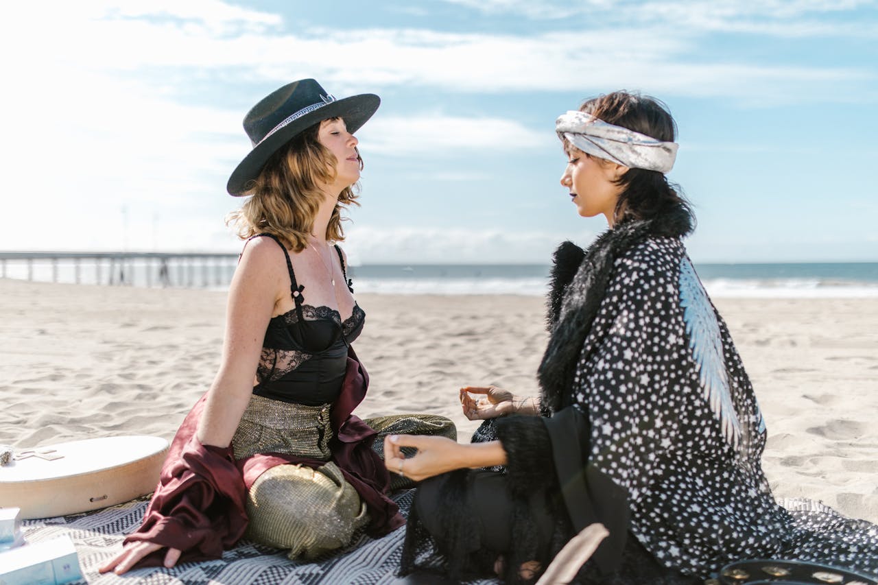 Two women meditating on a beach, embracing spirituality and mindfulness under a clear blue sky.