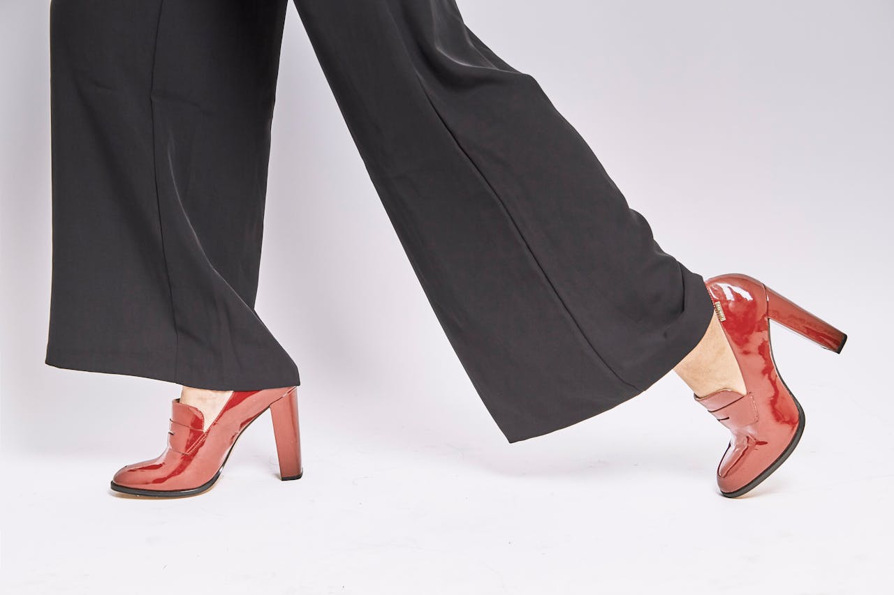 Stylish red high heels paired with black pants on a clean white background.