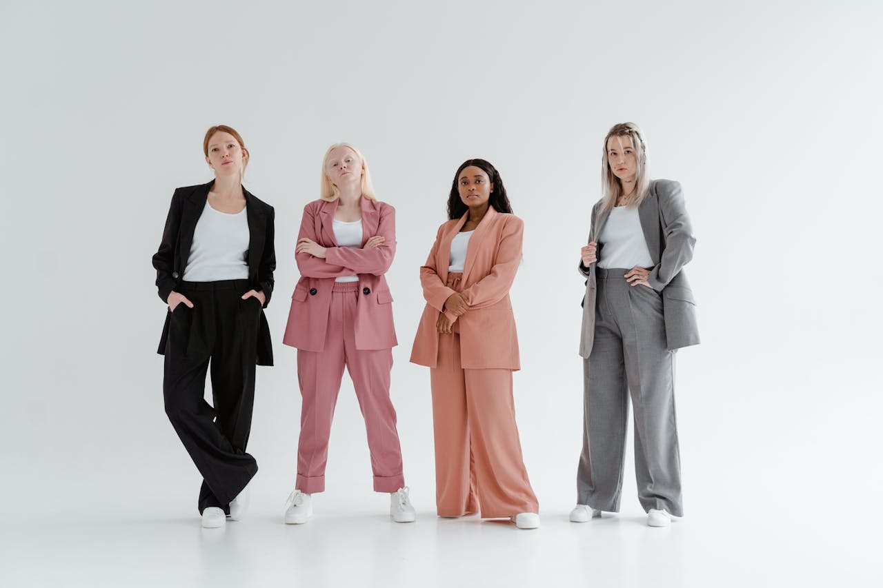 Four women confidently pose in colorful suits on a white background, showcasing modern fashion.